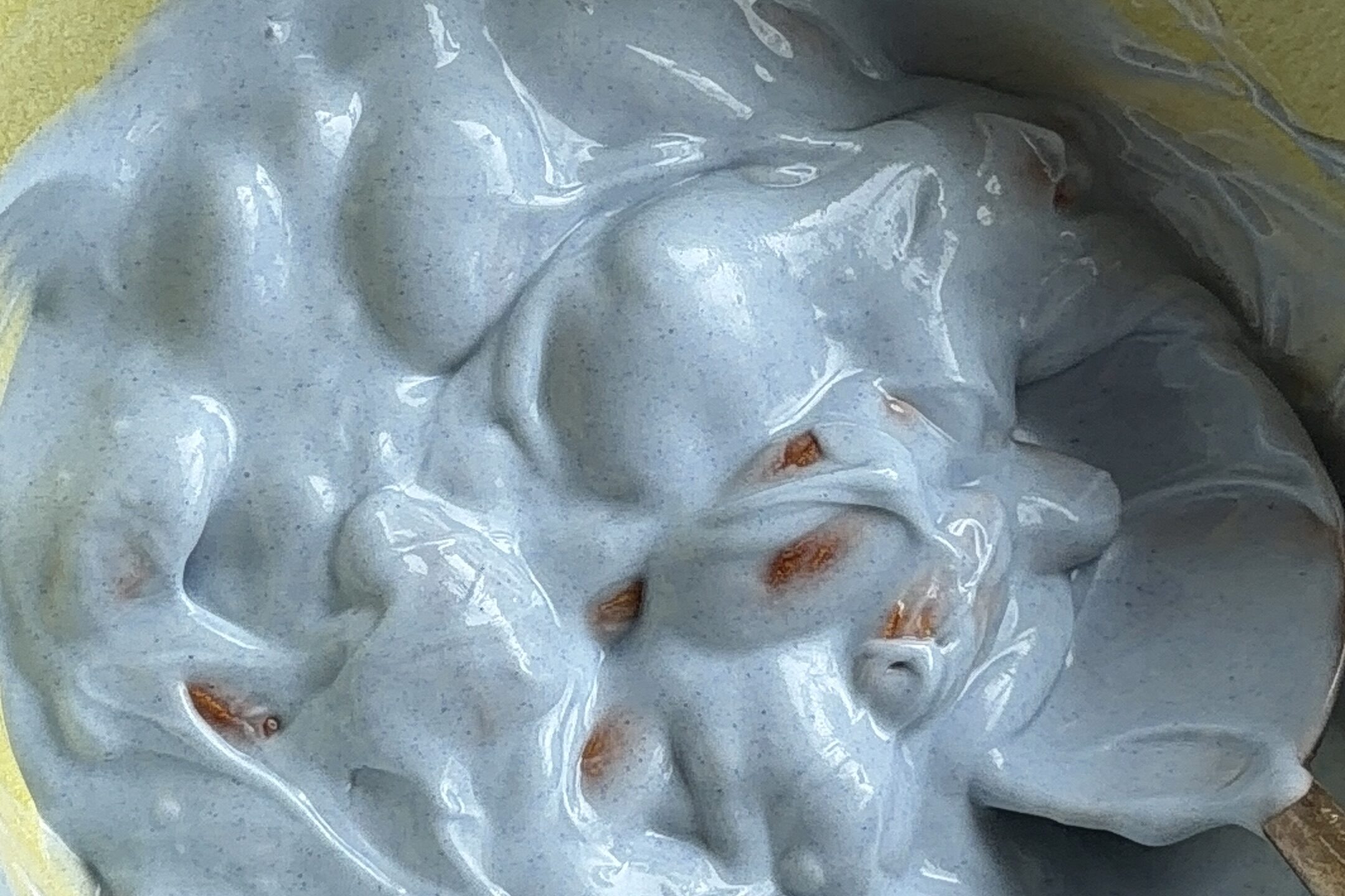 Almond mixed in a yellow bowl of white chocolate and blue spirulina mixture.