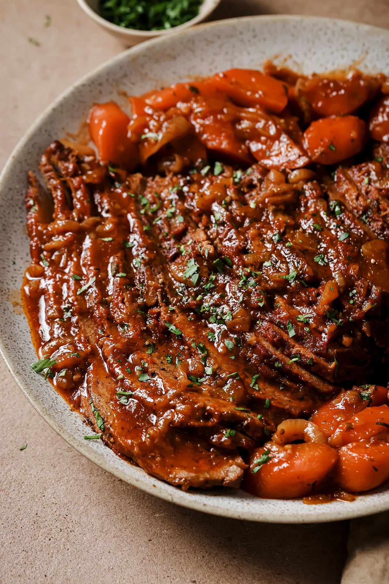 A speckled grey bowl with sliced brisket and veggies on it.