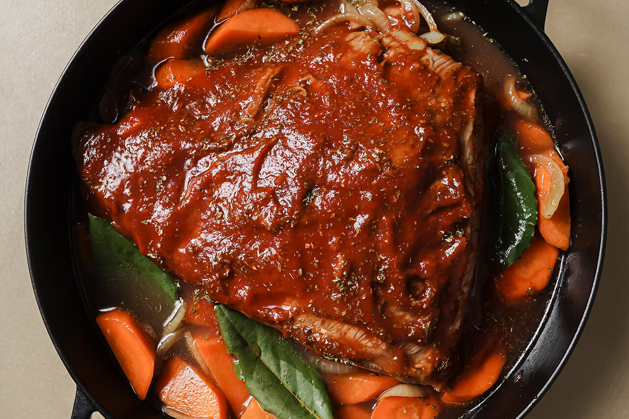 The brisket on top of veggies in the cast iron skilet topped with coconut sugar, tomato sauce and parsley.