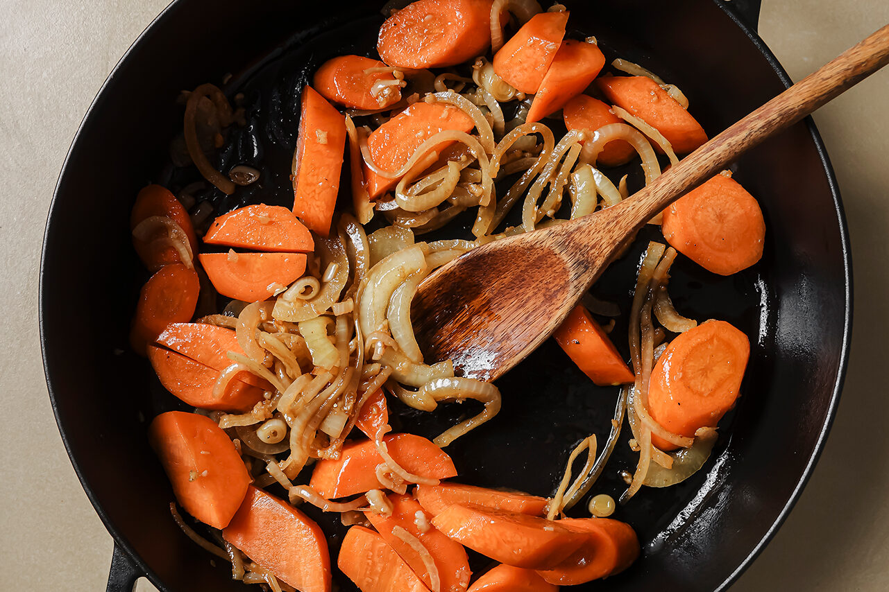 Carrots, onions, and garlic being sauted in a cast iron skillet.