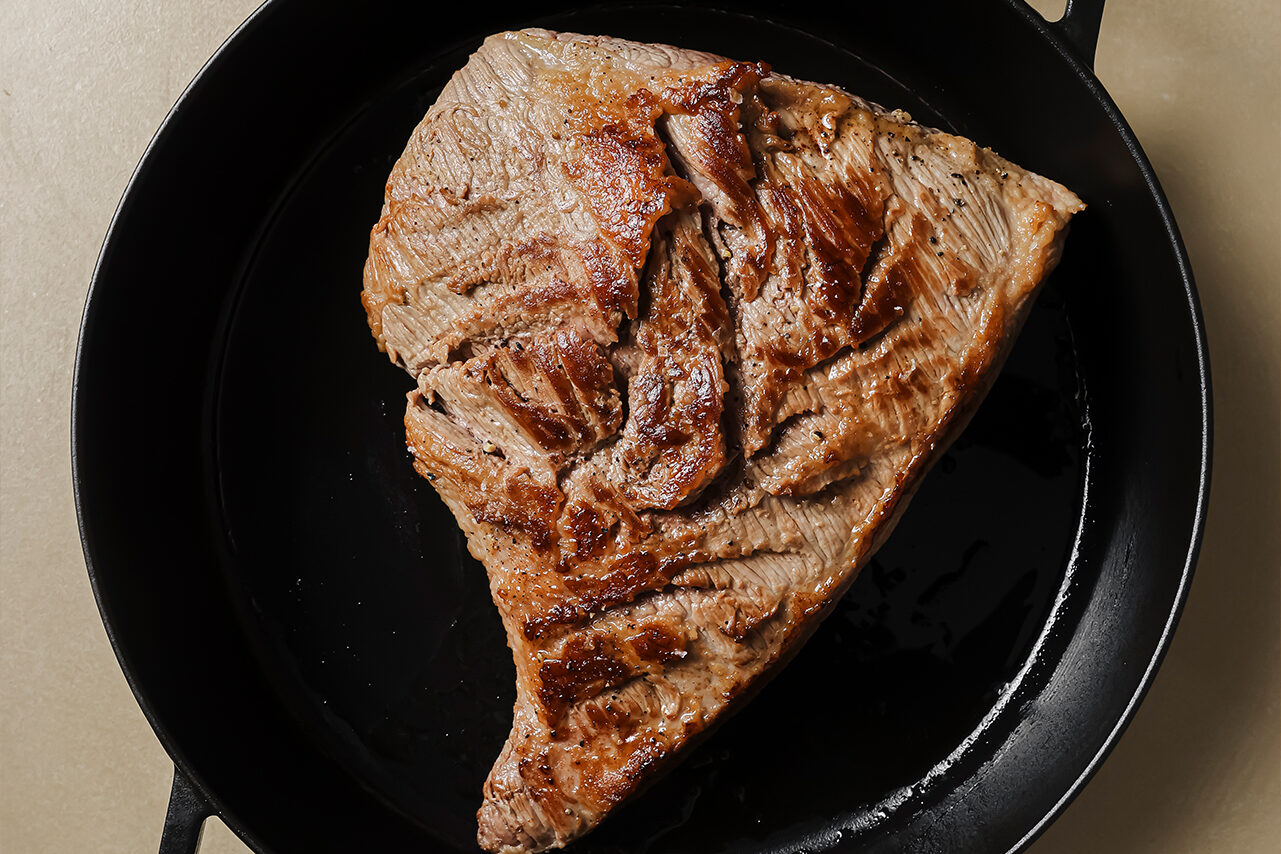 The brisket in a cast iron skillet searing.