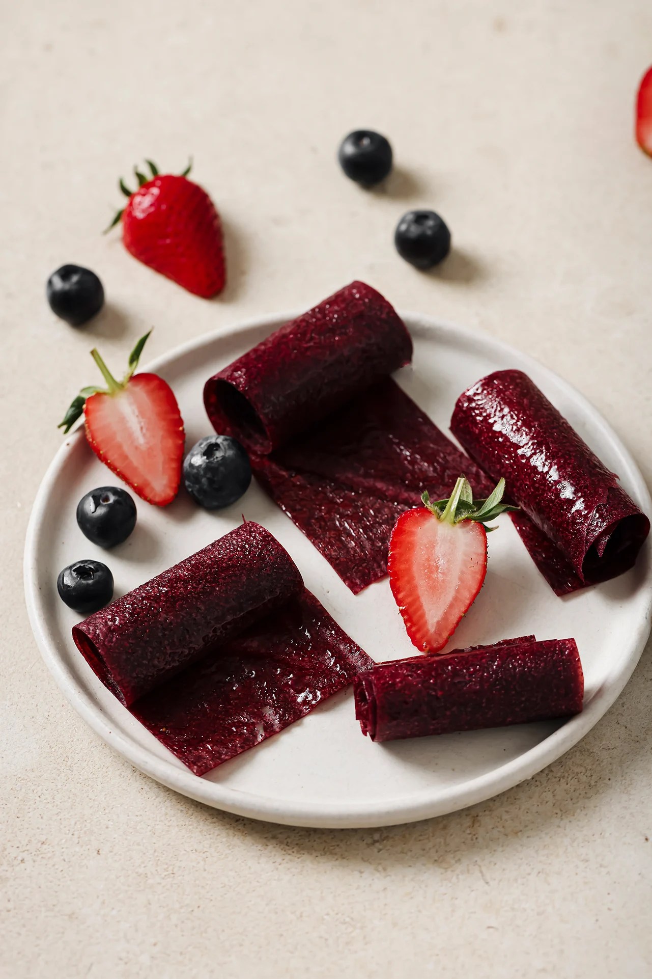 Fruit roll ups on a white plate with fresh berries.
