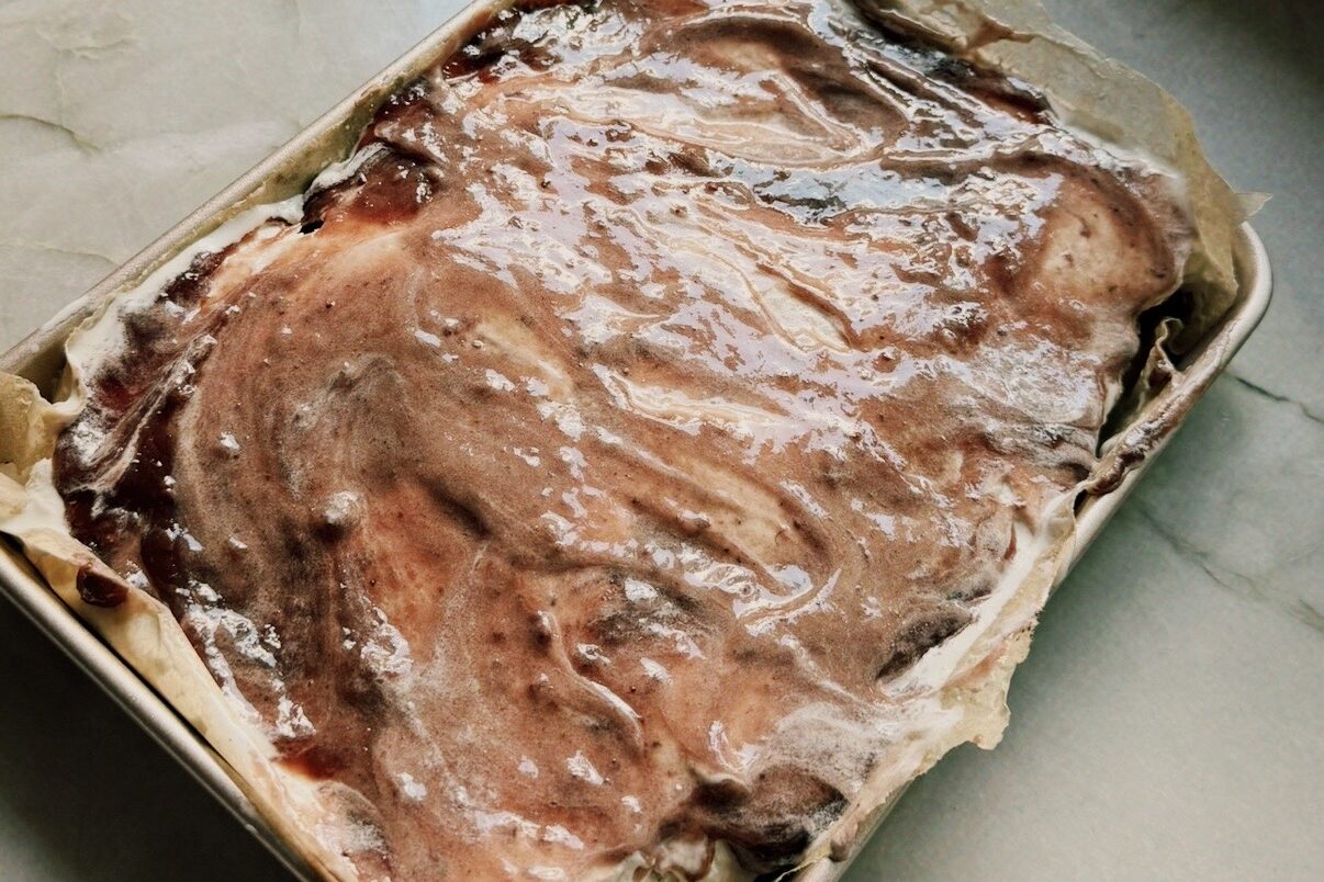 Rectangular cake pan topped with ice cream and ja,