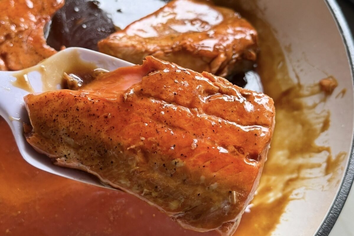 Teriyaki salmon being lifted out of a pan with extra sauce.