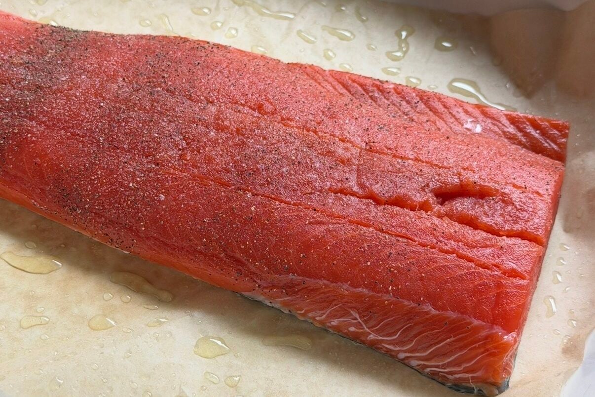 Salmon cooking in a pan lined with parchment paper.