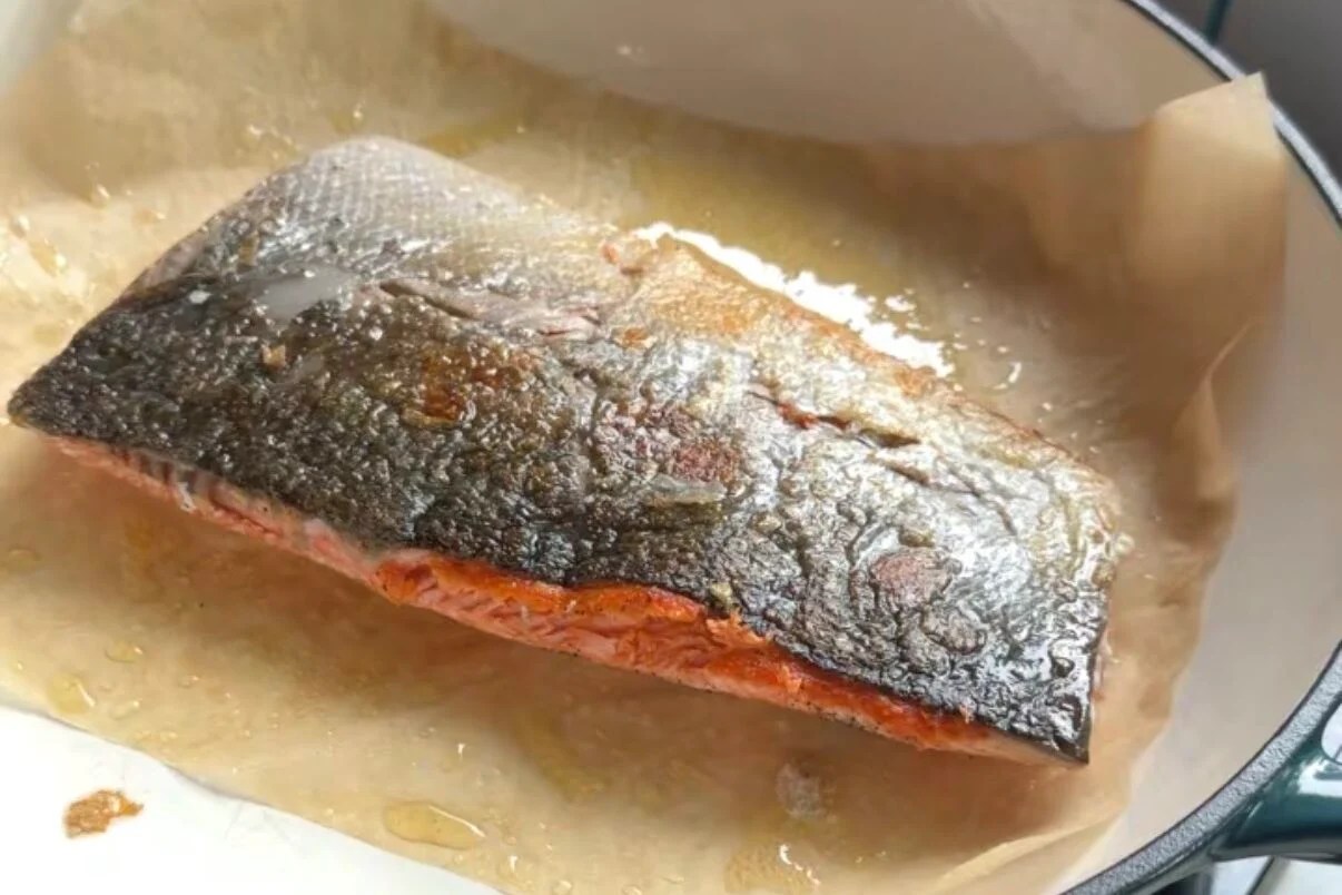 Salmon cooking in a pan with parchment paper.