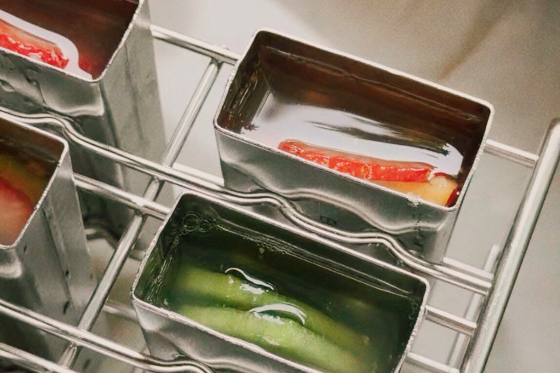 The popsicle molds with fruit and liquid in them before freezing.