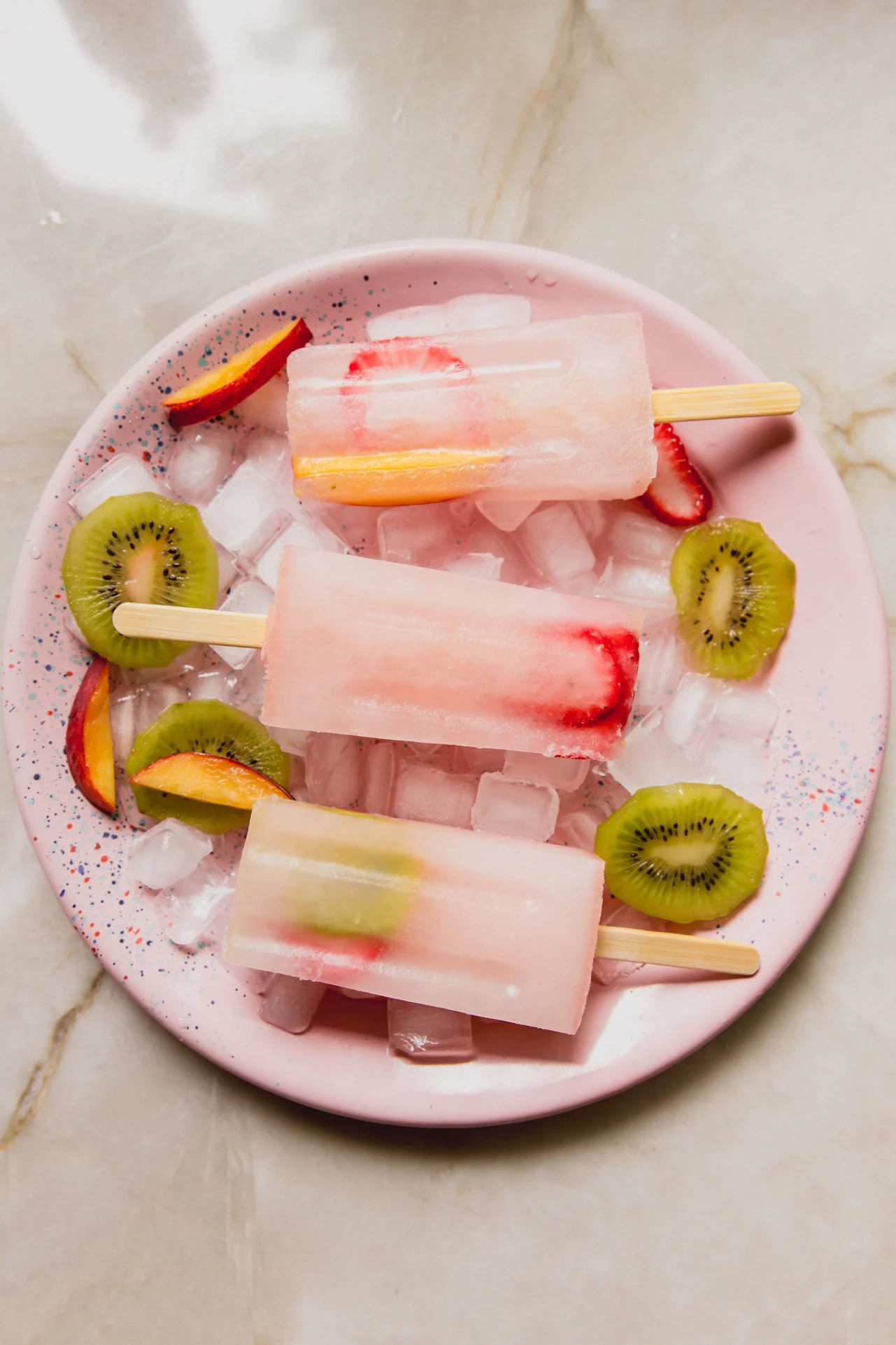 Three ginger and fruit popsicles on a pink plate.