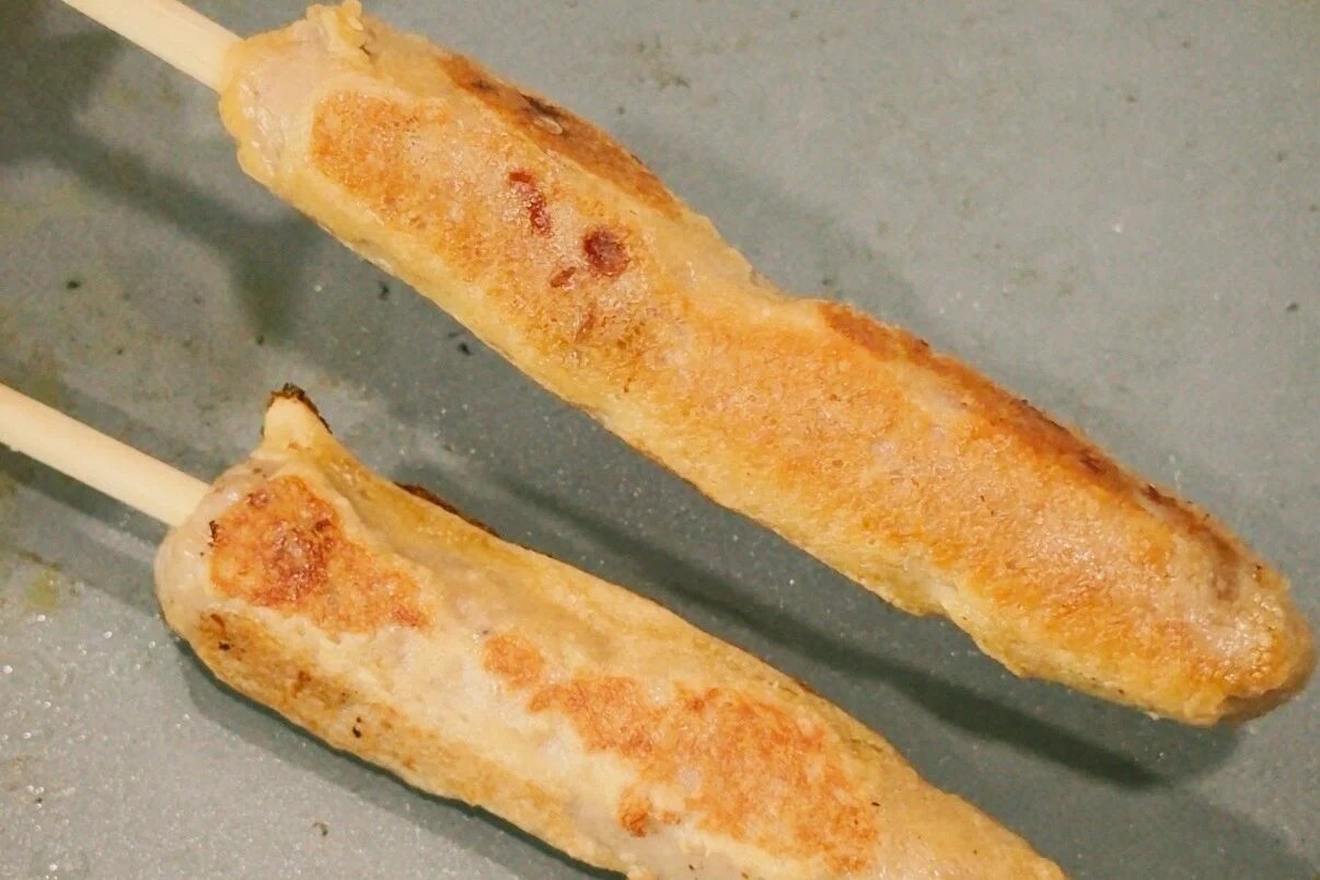 Two chicken sausage pancake skewers cooking on a nonstick pan after turning it.