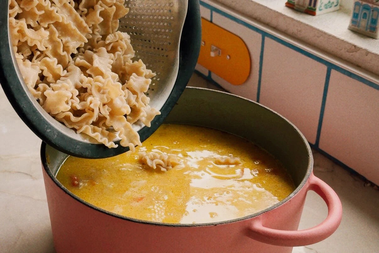 The cooked pasta being poured from a strainer into the soup.