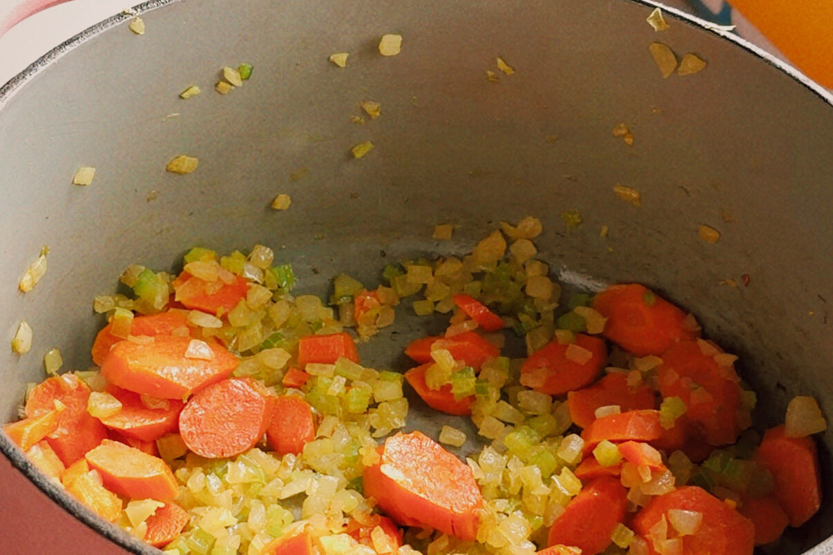 Onion, celery, and carrots sauting in a pot on the stove.