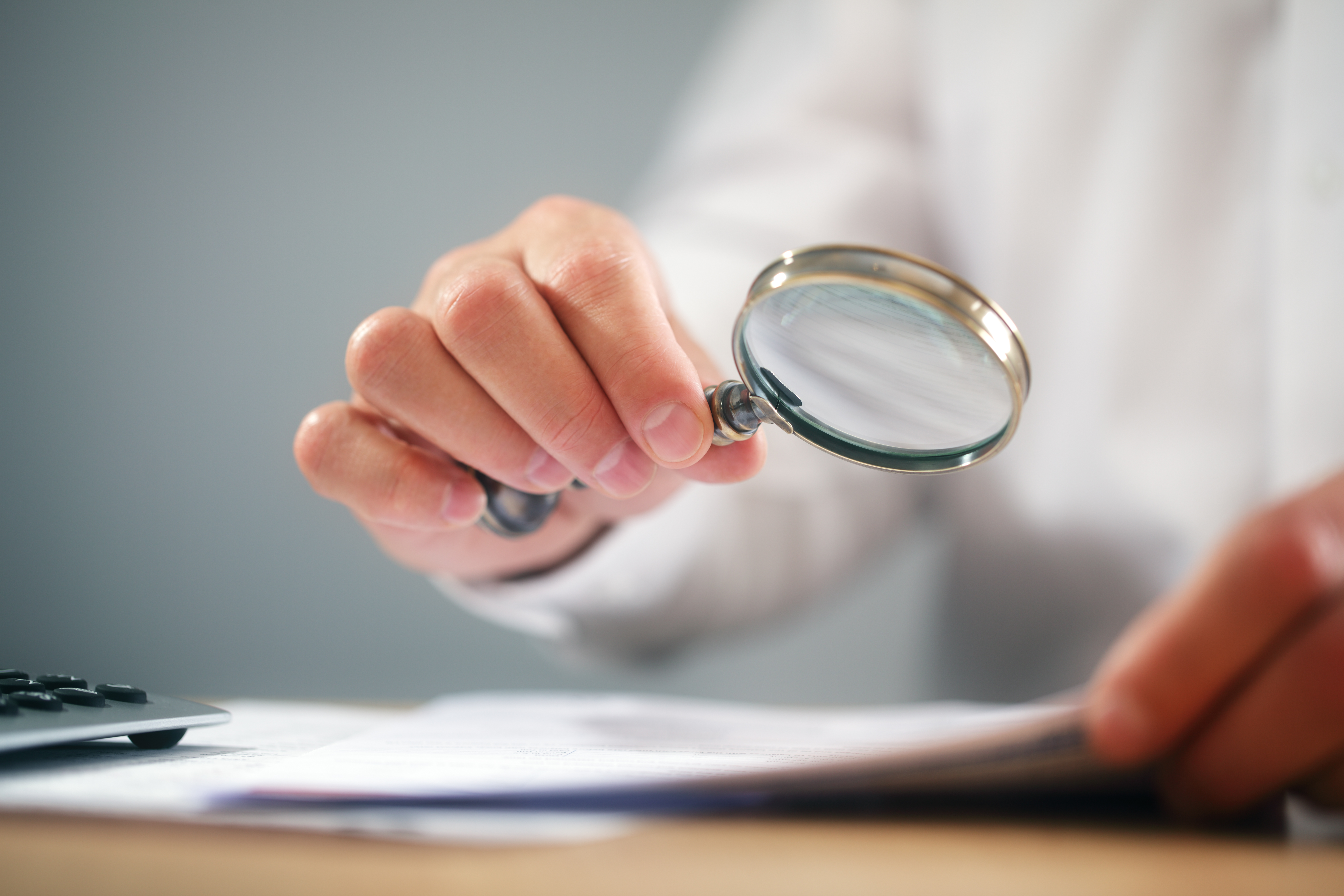 Businessman with magnifying glass reading documents Go From Stress To