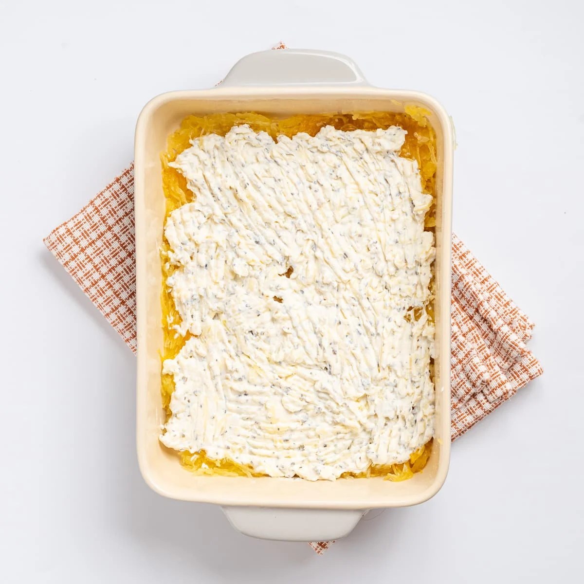 An image of a layer of the ricotta cheese mixture spread on a baking sheet, with the layer of spaghetti squash slightly visible beneath it.