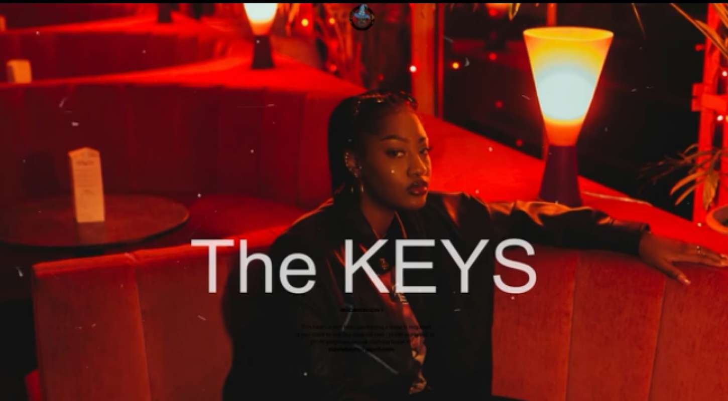 Singer Tems sitting and leaning left hand on the table. [Inscription] the Keys