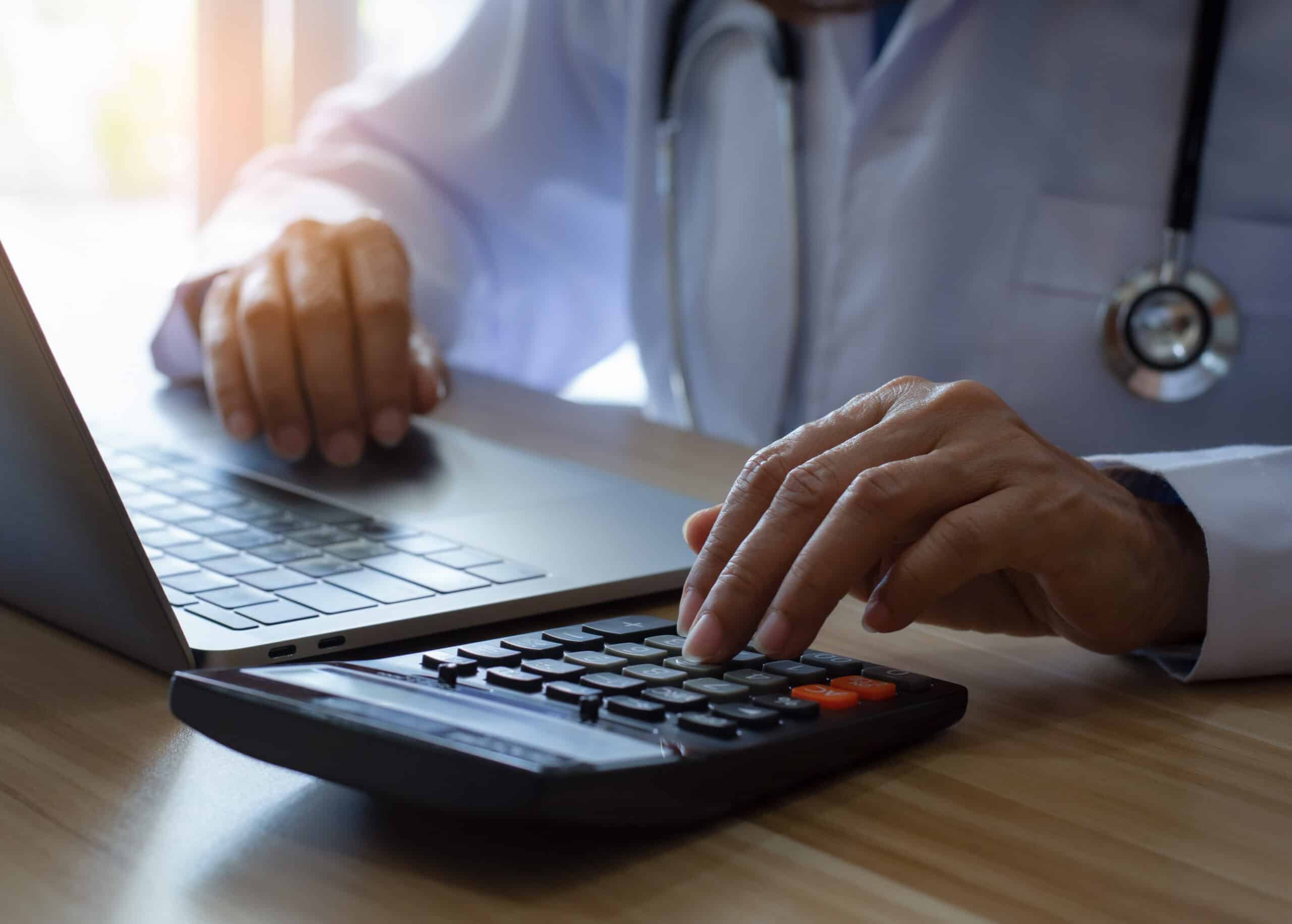 Doctor or physician using calculator and work on laptop computer at
