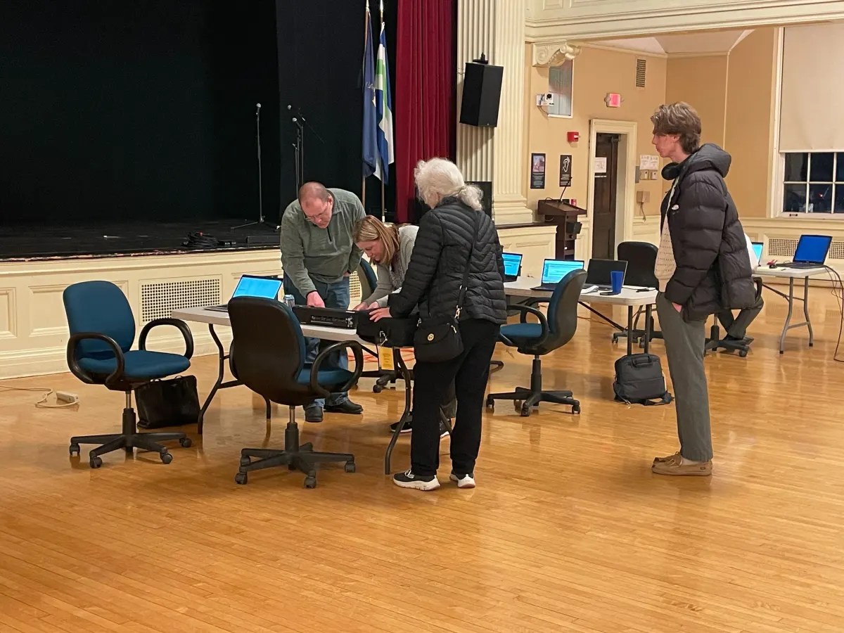 A group of people standing in a room with chairs and laptops.