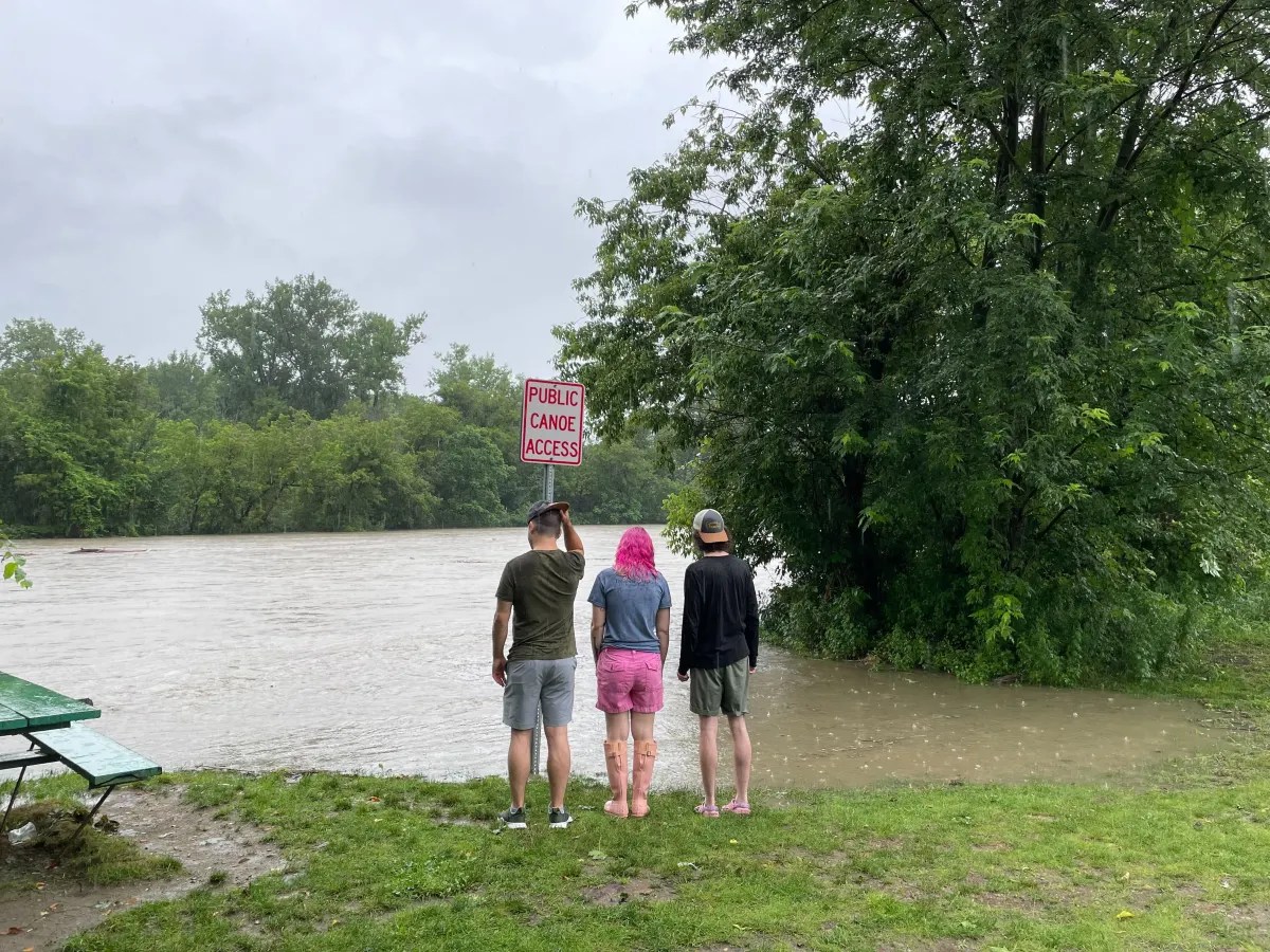 three people standing next to a river with a sign in front of them.