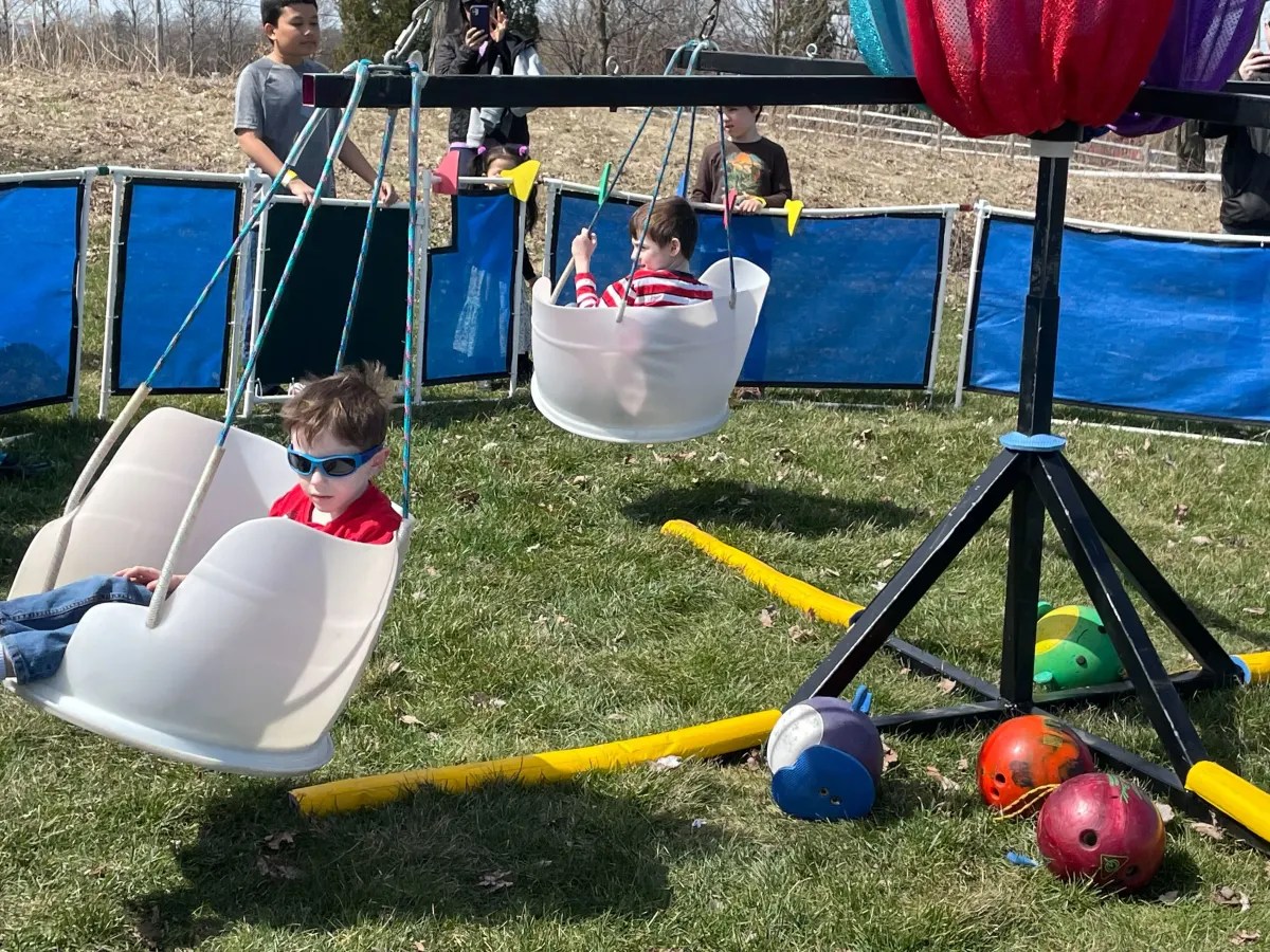 Children enjoying a swing ride at an outdoor event with scattered toys on the ground.