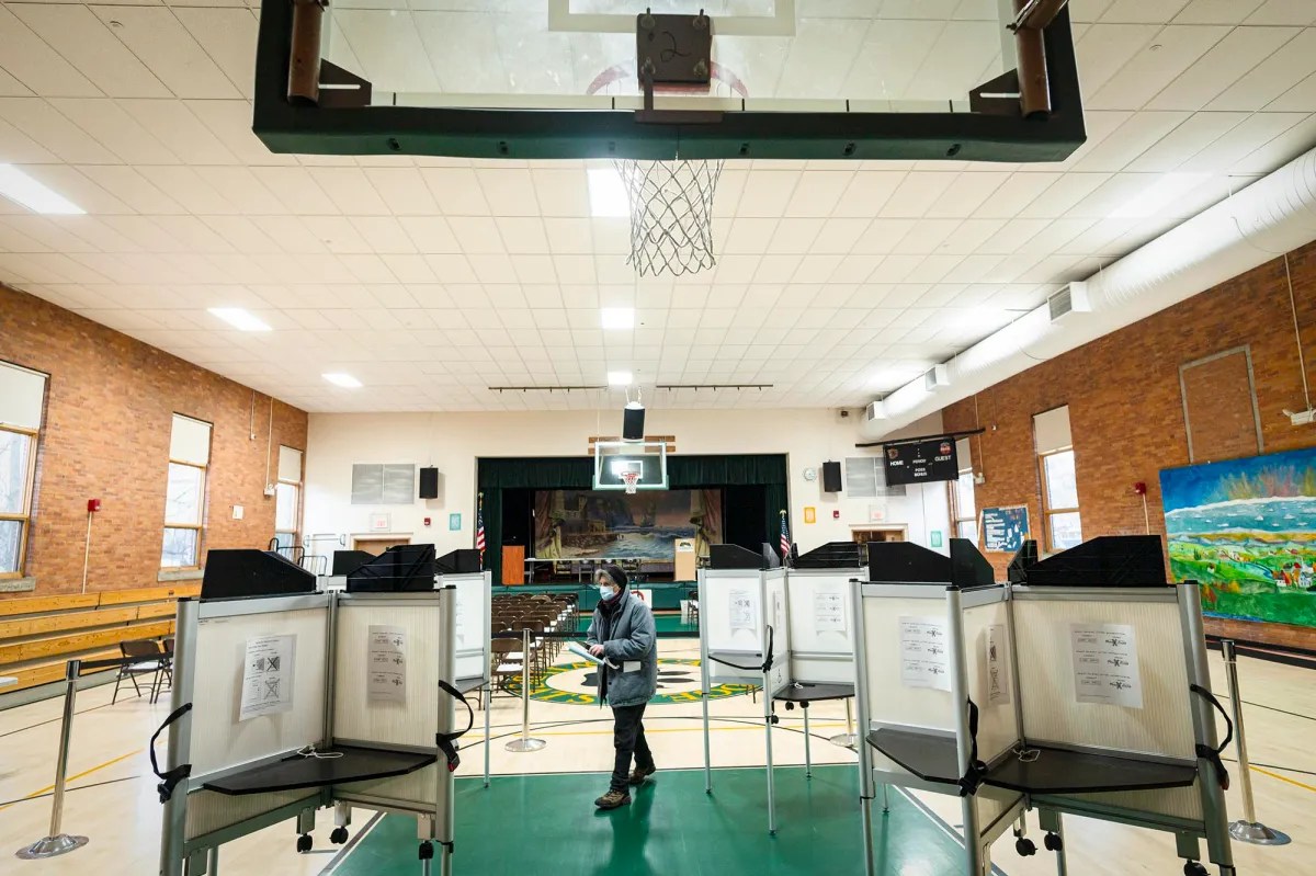 A person standing in front of voting booths in a gym.