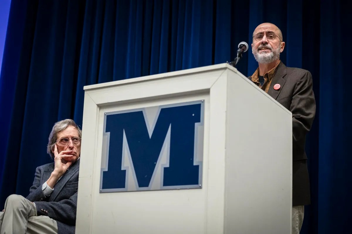 Two men standing at a podium in front of a m sign.
