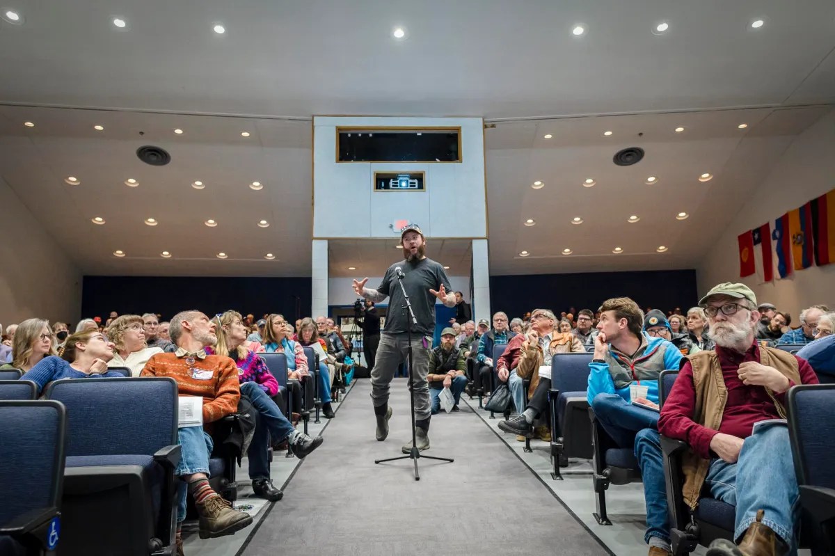 A man speaks to a crowd of people in a large auditorium.