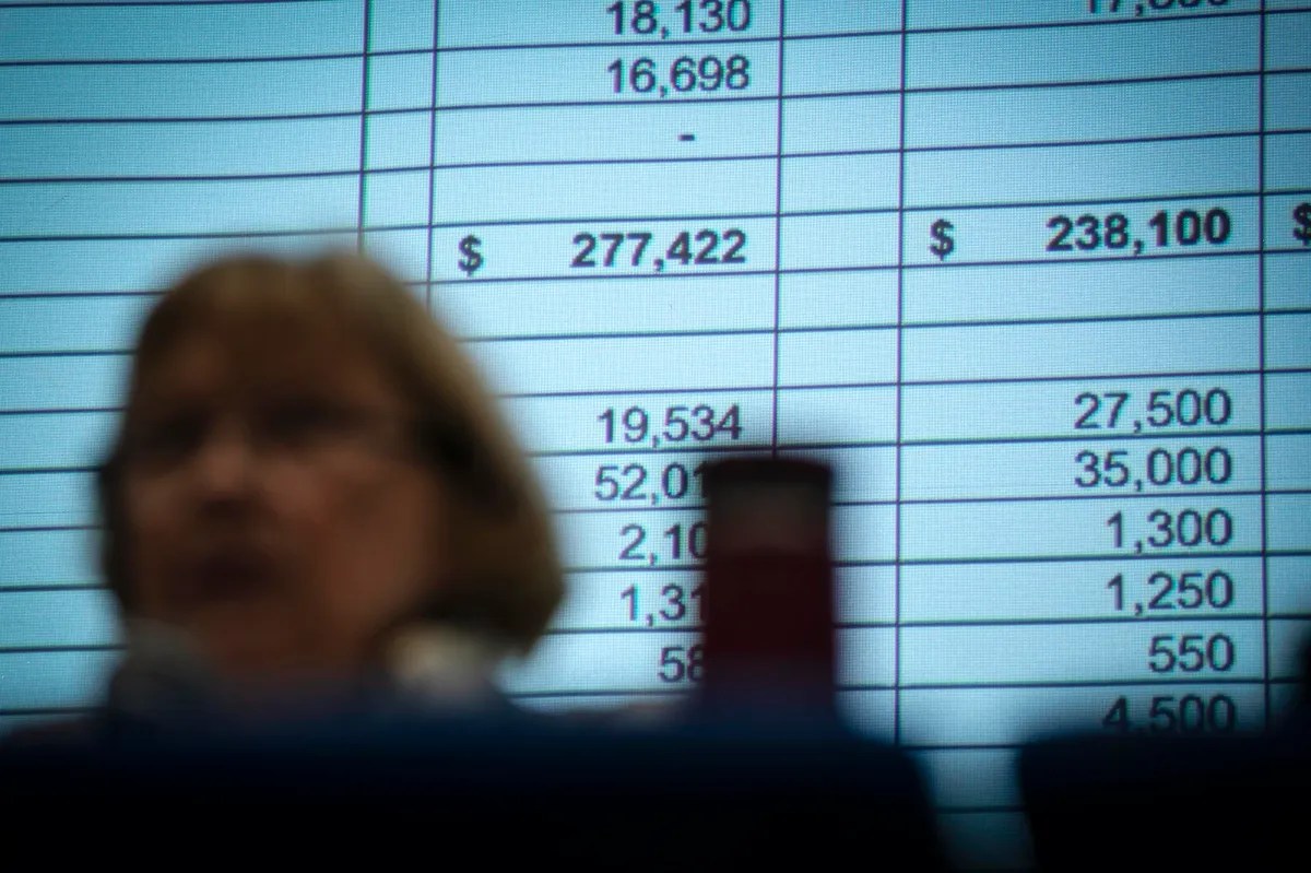 A woman is standing in front of a screen with numbers on it.