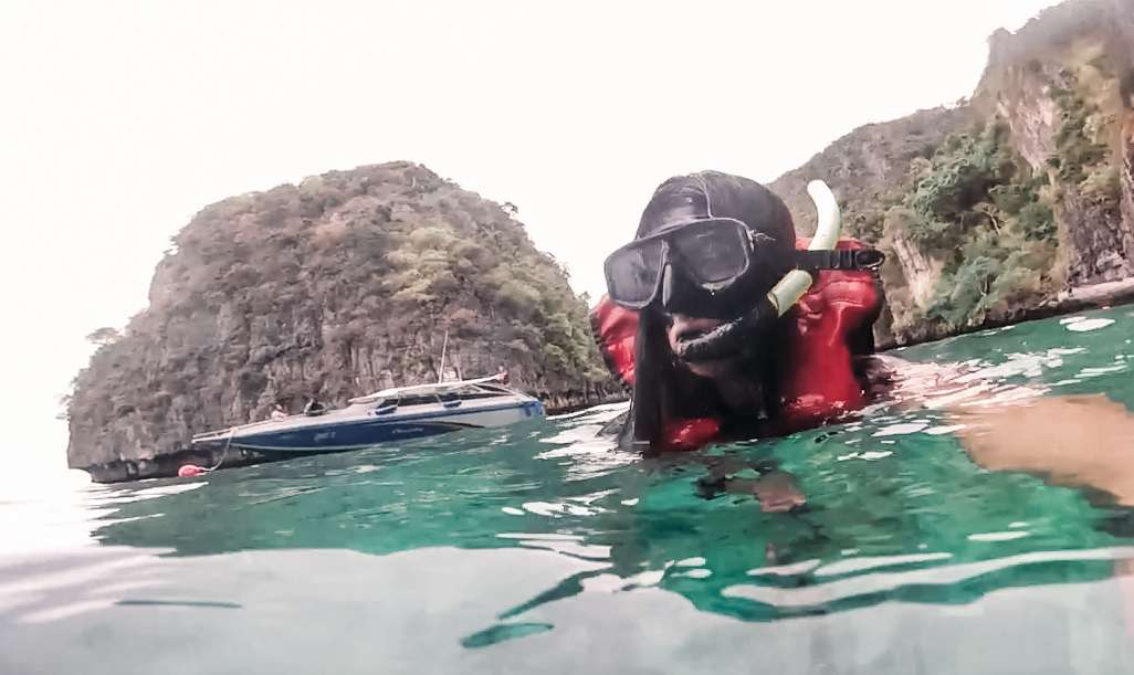 Woman snorkeling in turquoise water with a speedboat and trees in the background.