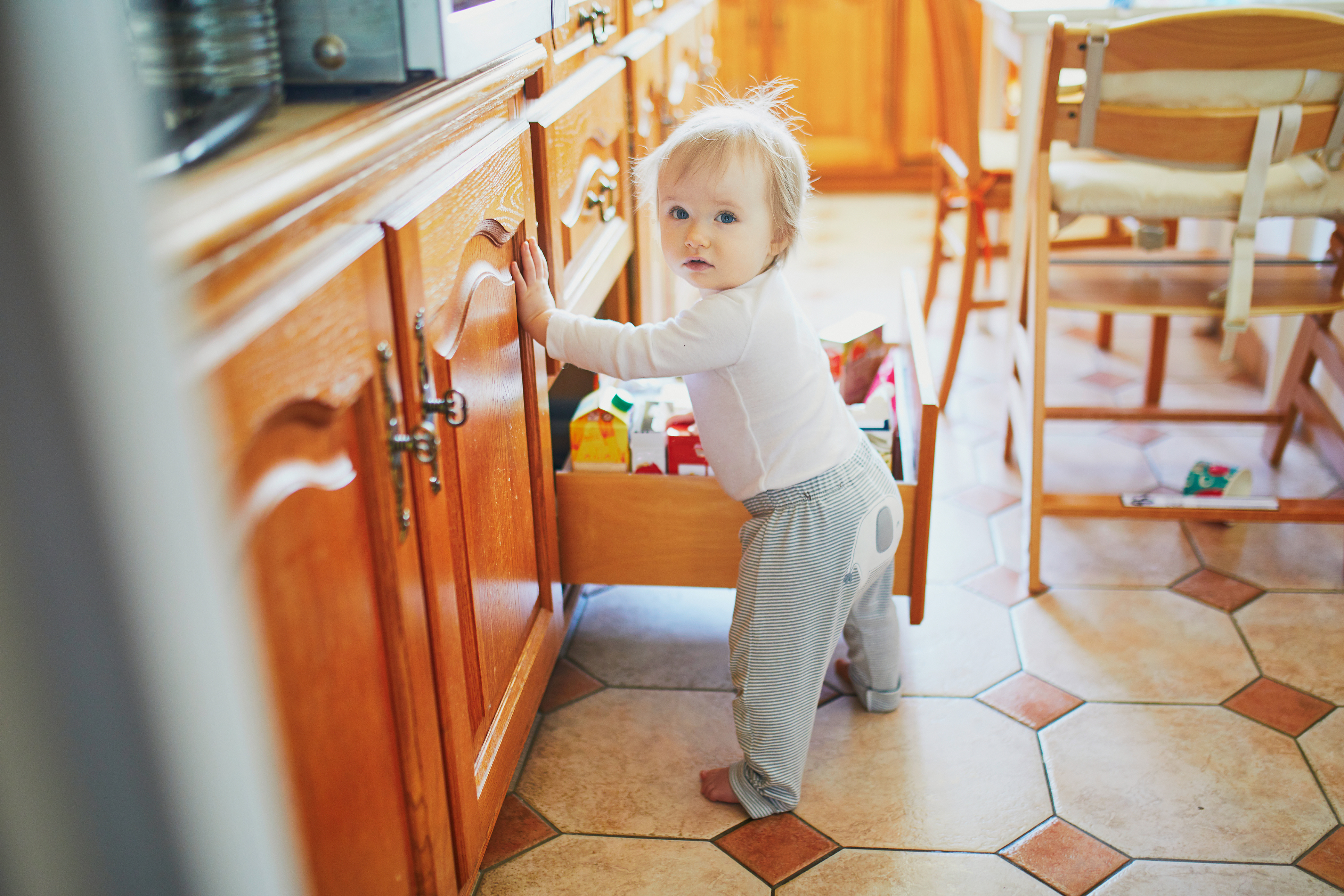 Adorable toddler girl at home, opening the drawer in the kitchen Window Covering Safety Council