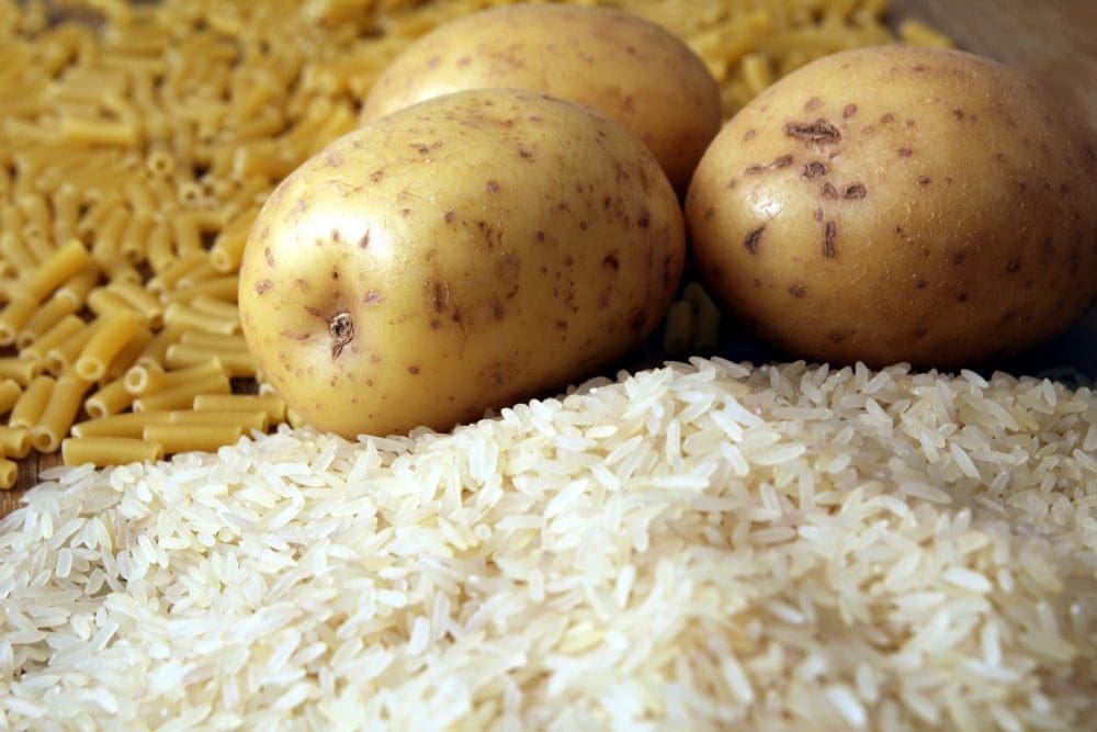 Rice, potatoes and macaroni pasta on a wooden table.Three common