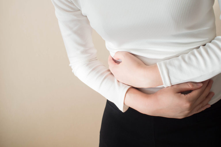 Young female suffering form stomach ache on gray background w/ copy