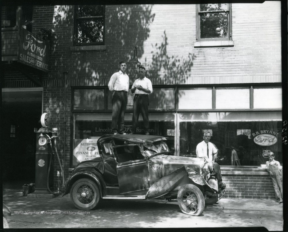 Odd Photo of Two Men Standing Atop a Wrecked Car in front of B.B