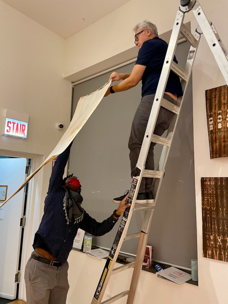 Quincy handing the short end of a banner to Larry, who is on a ladder