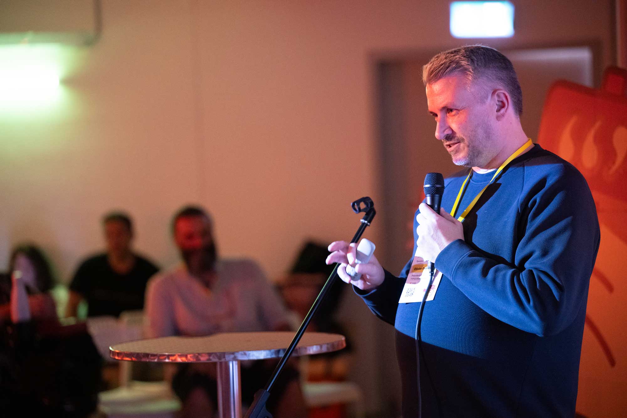 Alt Ctrl Org Draws 200+ for Open Discussion on WordPress, Free Software, and Governance 2 A speaker holds a microphone while addressing an audience in a dimly lit room.