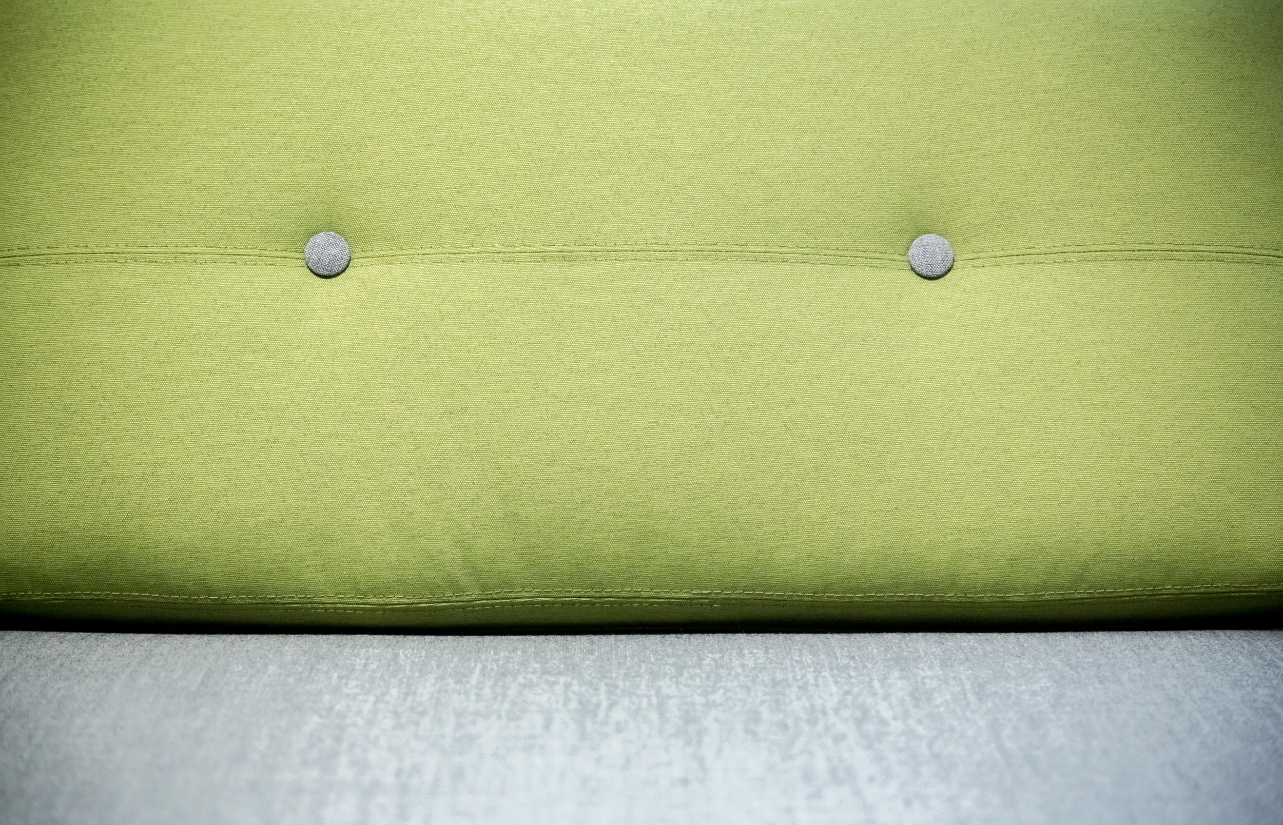 Close up of a sofa with a green cushioned back and a light grey seat.