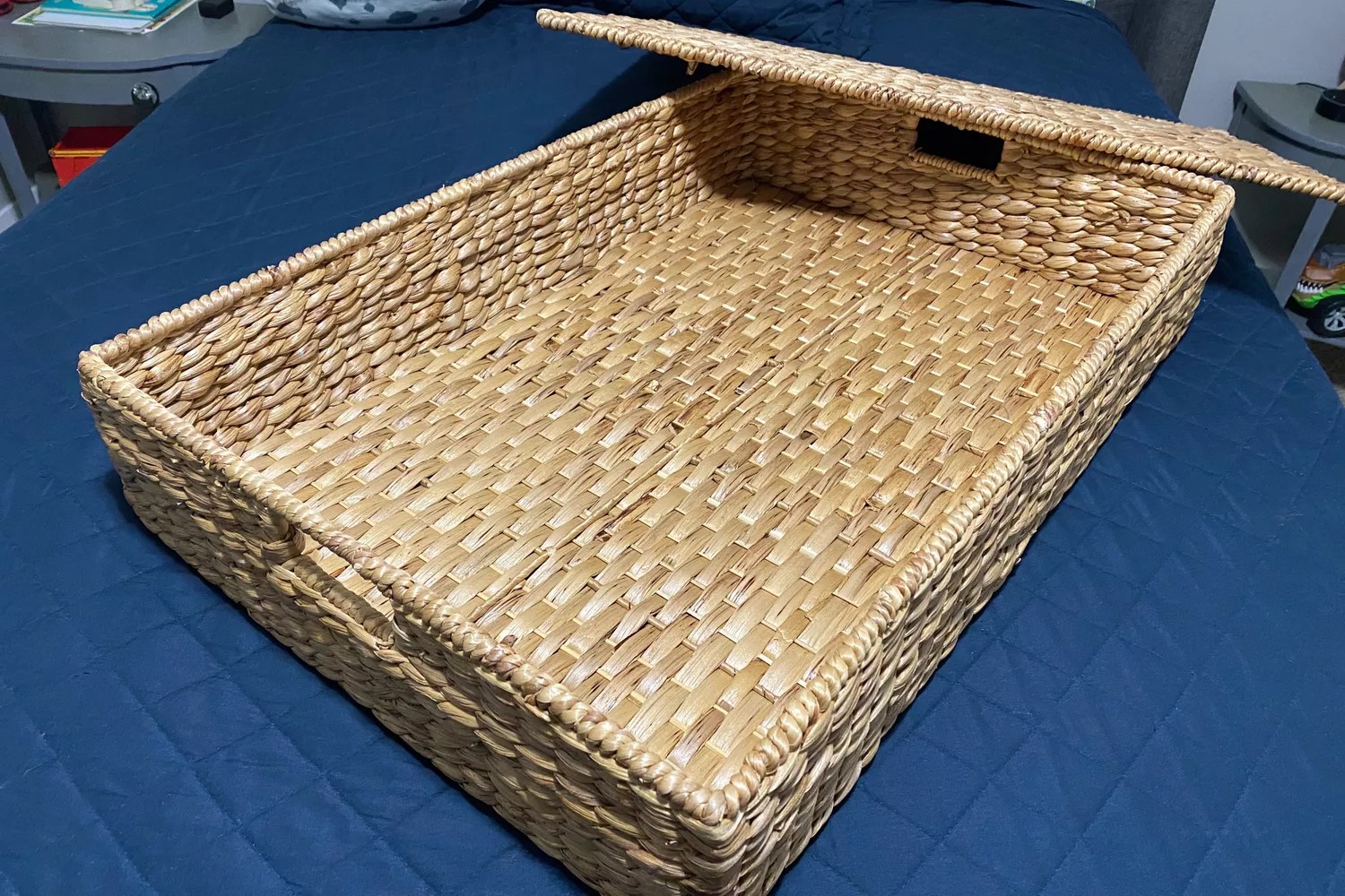 The Pottery Barn Savannah Handwoven Seagrass Lidded Underbed Basket on top of a bed