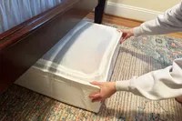 A person pushing the IKEA SKUBB Storage case under a bed with a wooden frame