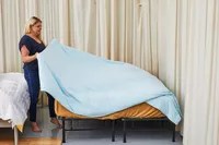 A person holding one side of the Rest Evercool Cooling Comforter on a bed
