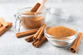 ground cinnamon in clear bowl with cinnamon sticks on counter