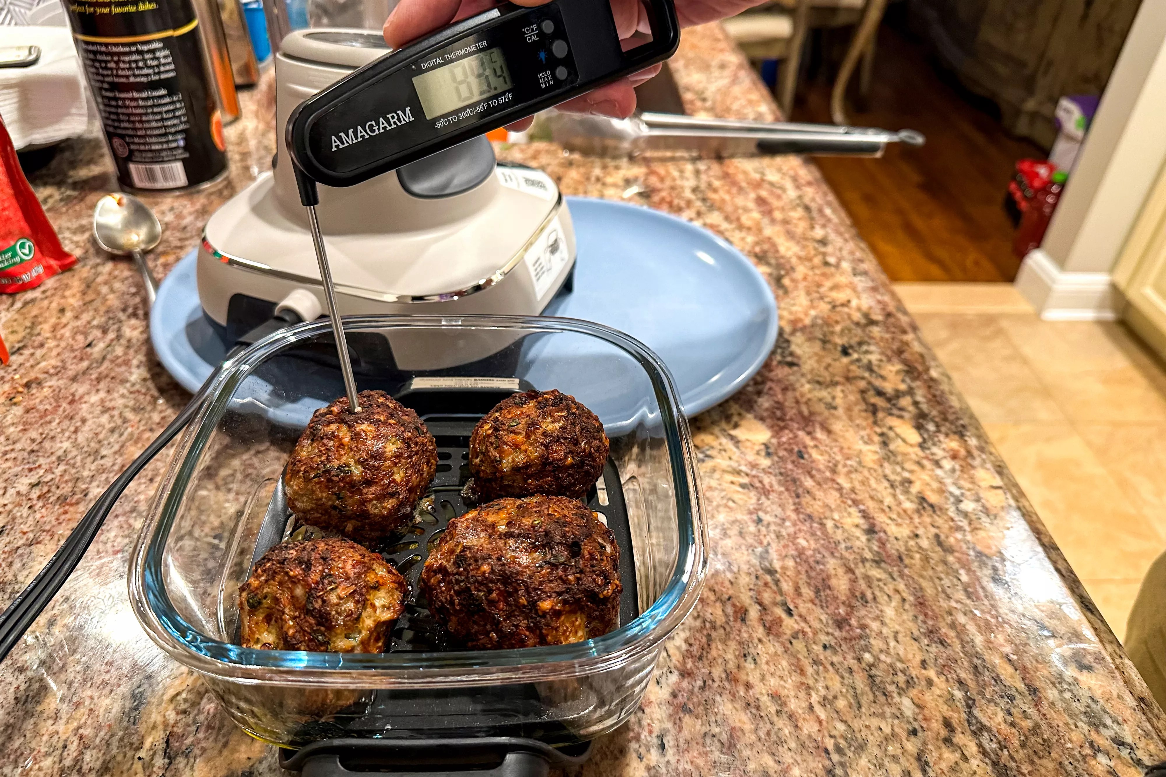 A person tests the temperature of burgers cooked in the Ninja Crispi Air Fryer