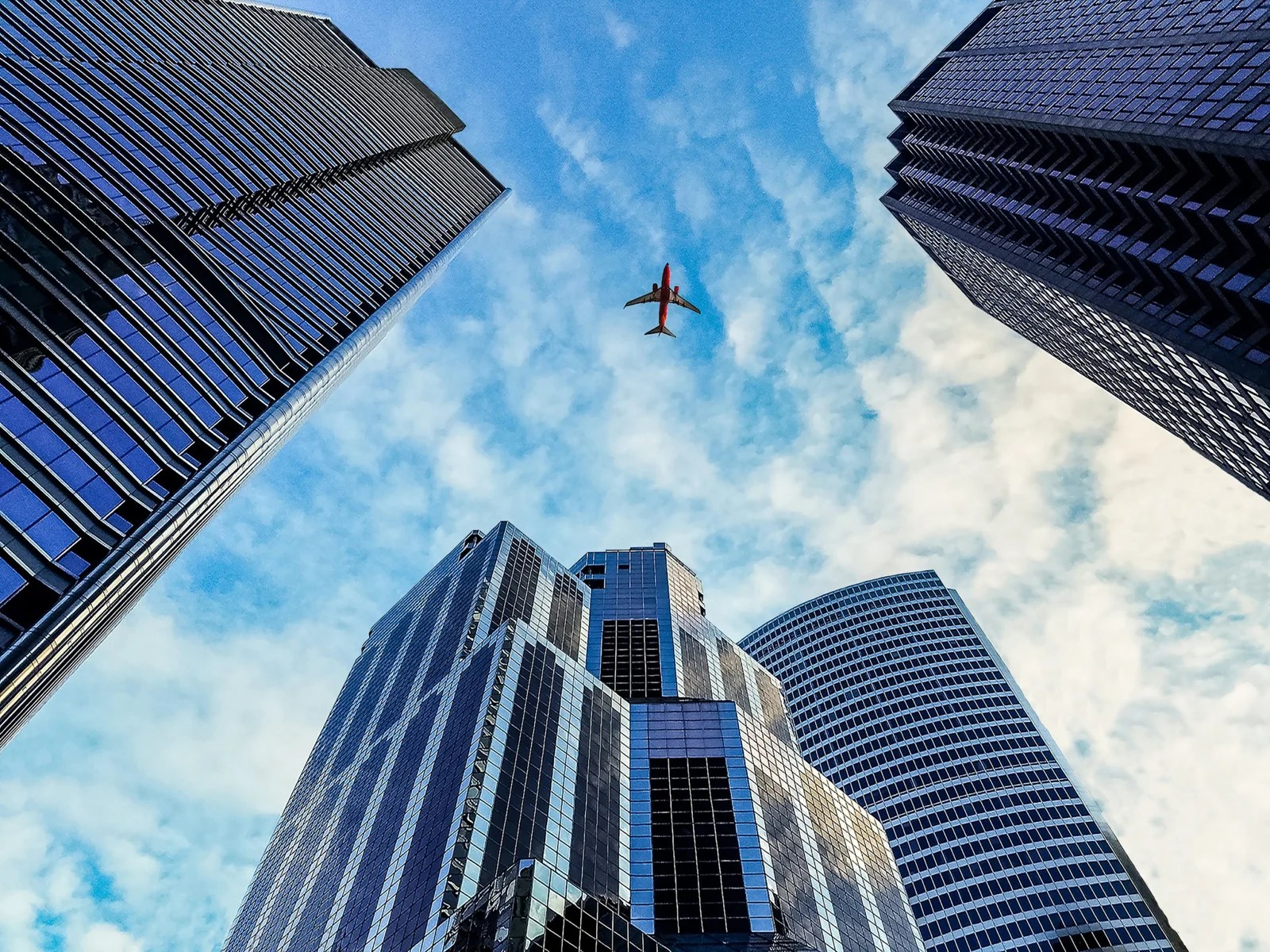 worm's eye view of airplane passing by buildings