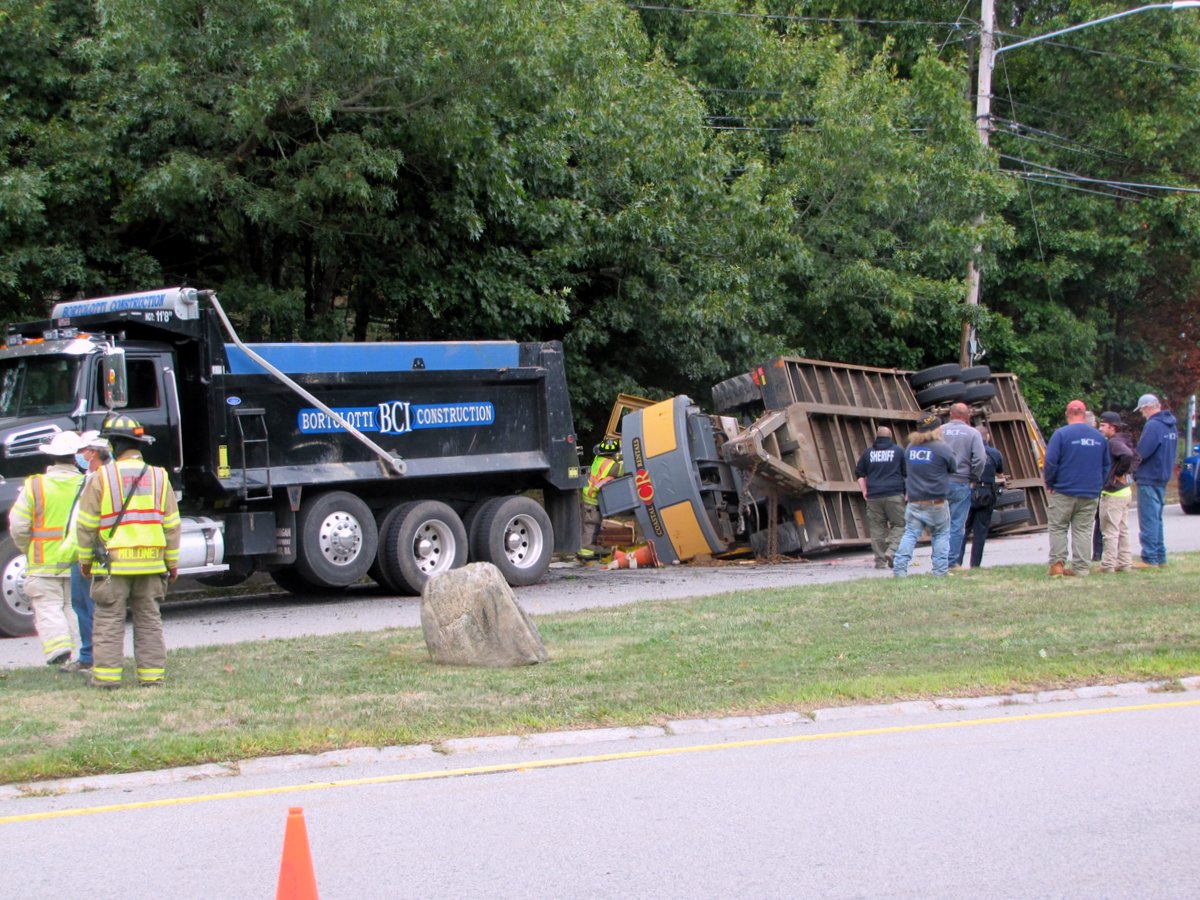 Trailer with excavator being towed by dump truck rolls over in West