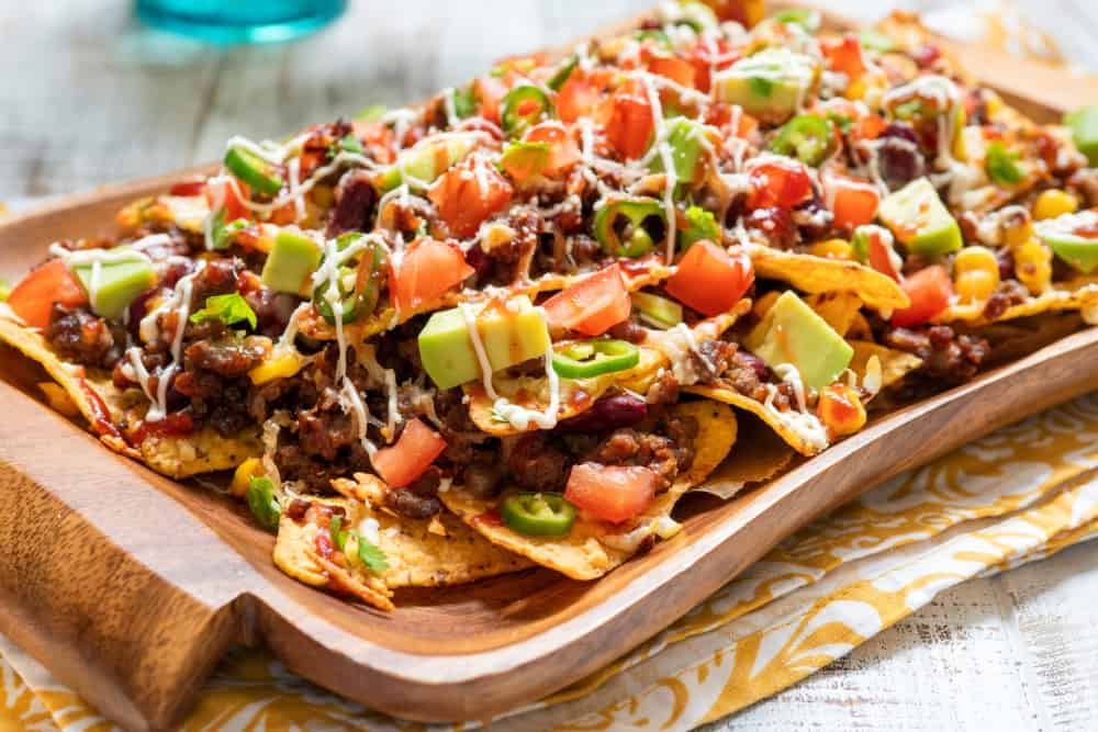 Nacho corn tortilla chips with cheese, meat, guacamole and red hot