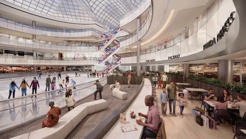 A spacious shopping mall with people dining at a café and others ice skating. The mall features multiple floors, a glass ceiling, and a lively atmosphere.