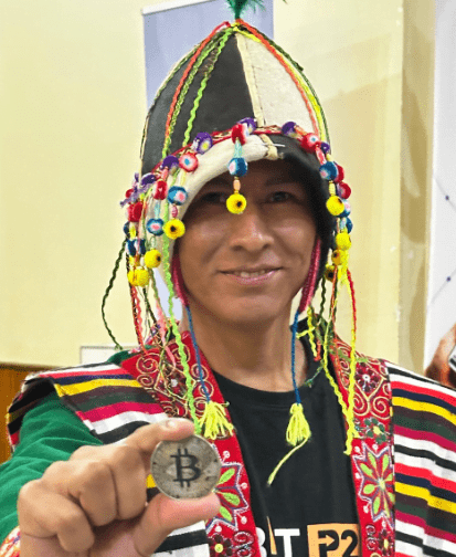 Une personne vêtue d’un costume typiquement bolivien montre une pièce physique en bitcoin.