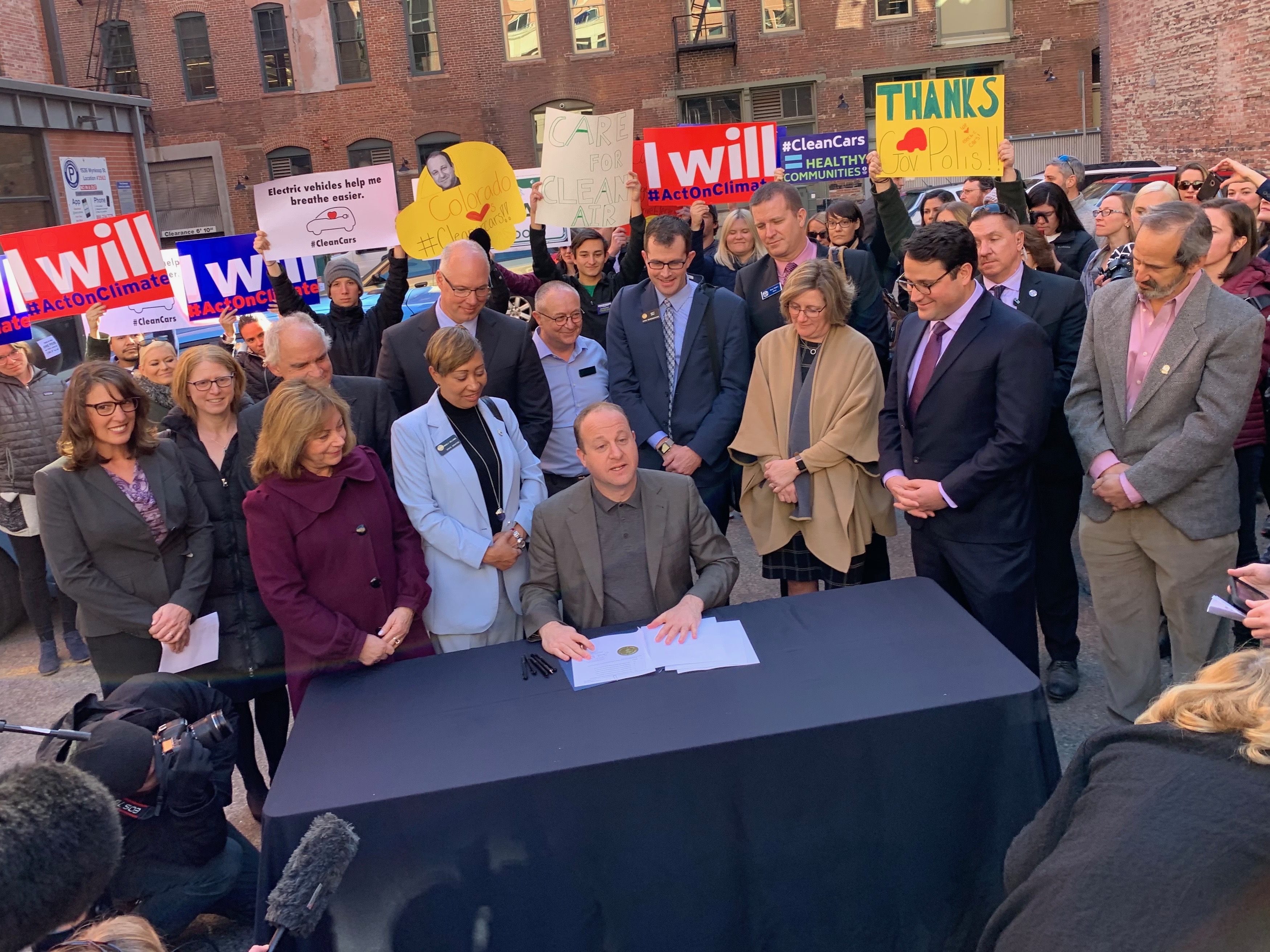 Colorado Gov. Jared Polis, center, signs an executive order promoting zero emission vehicles Thursday in downtown Denver.