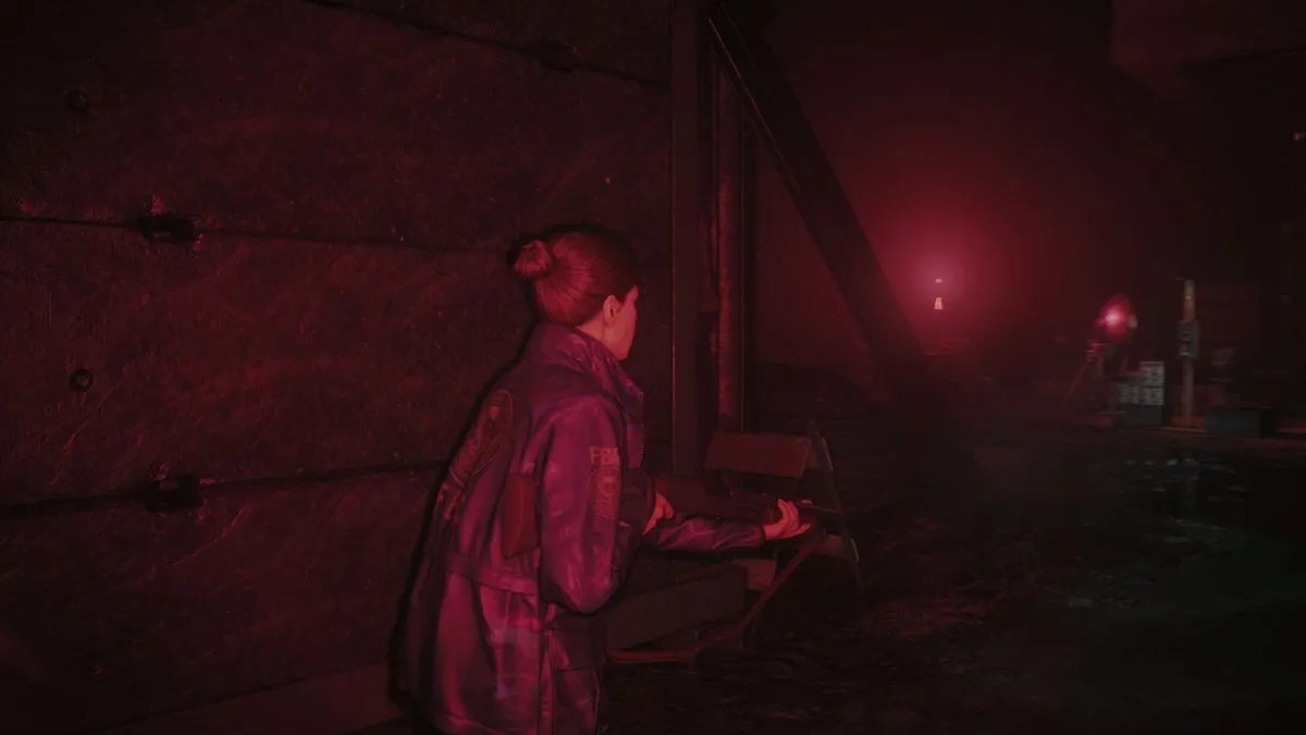 Kiran Estevez stands with a shotgun in a creepy room lit with red