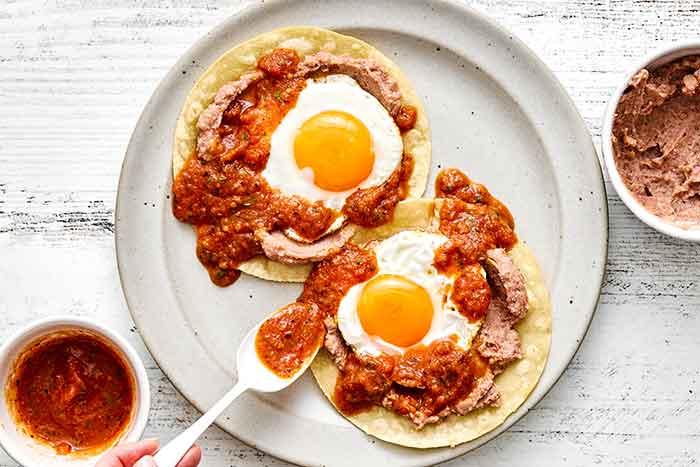 Adding ranchero sauce to huevos rancheros.