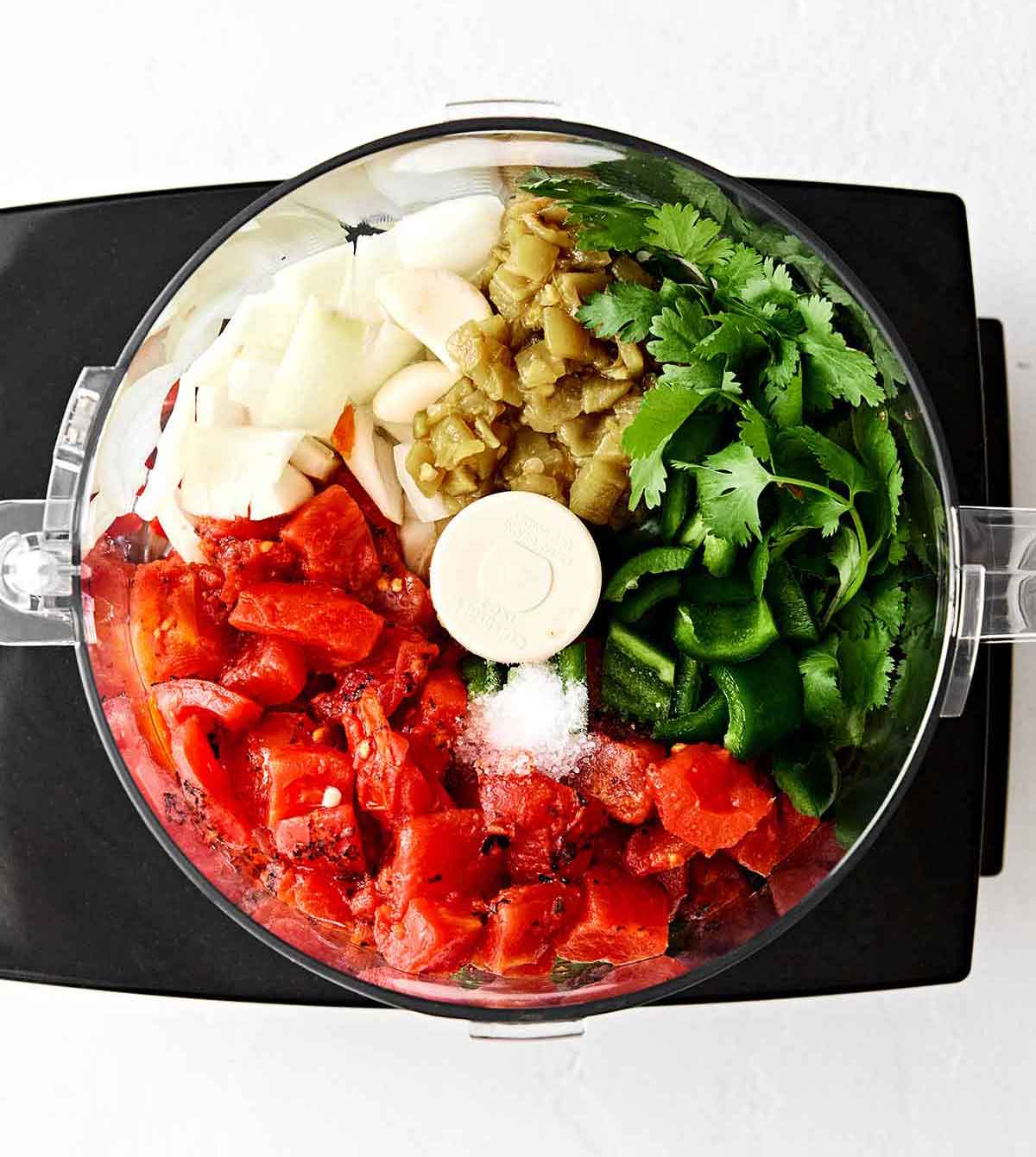 Nothing compares to this homemade restaurant-style salsa! It's blended enough to be saucy, but still a little chunky. Adding salsa ingredients to a food processor.