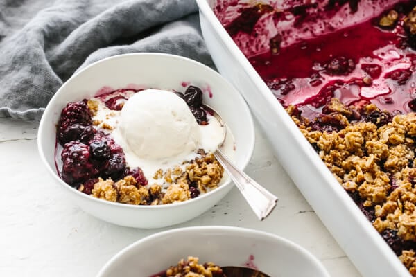 Berry crisp in a white bowl topped with ice cream.