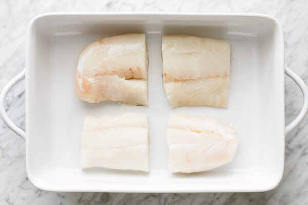 Raw cod filets in a baking dish.